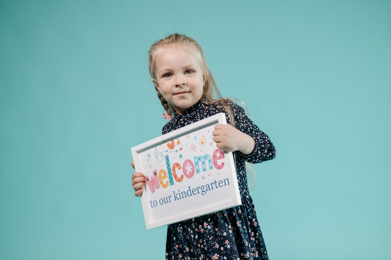 A cheerful girl poses with a welcome sign against a light teal background.